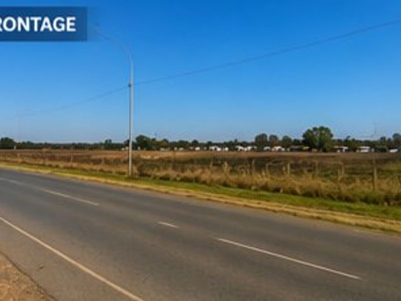 A view of the property road frontage showing the adjacent asphalt road, wire fencing, and open land.