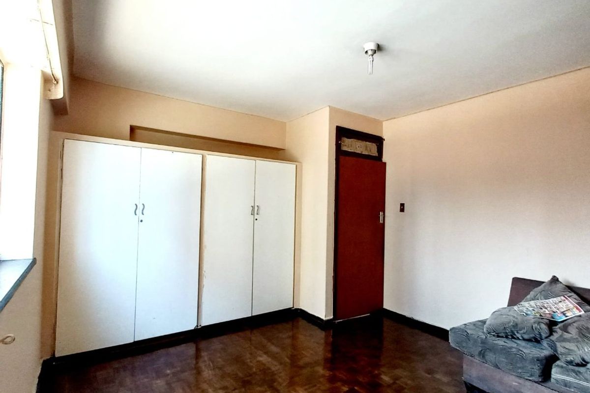 A bedroom featuring parquet flooring and built-in cupboards, offering a functional space with potential for cosmetic updates.