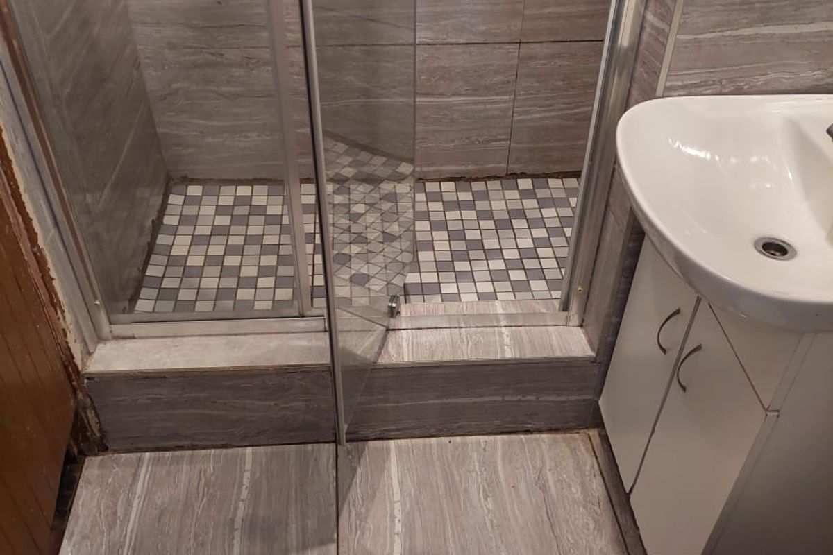 A compact bathroom featuring a glass-enclosed shower with mosaic floor tiles, a modern vanity basin, and a standard toilet with neutral wall tiling.