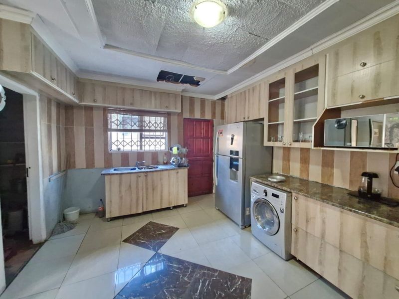 A functional kitchen featuring built-in cabinetry, granite countertops, and tiled flooring, currently requiring ceiling repairs and cosmetic updates to improve its overall condition.