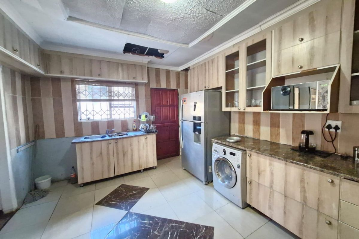 Kitchen featuring wood-look cabinetry, granite countertops, and tiled flooring. The space requires ceiling repairs and general cosmetic updates to modernize the finishes.