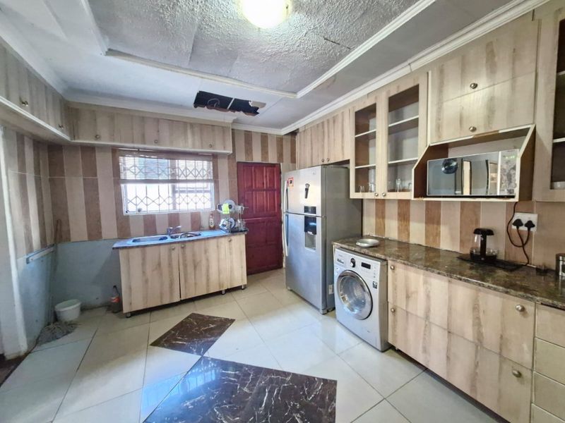 Kitchen featuring wood-look cabinetry, granite countertops, and tiled flooring. The space requires ceiling repairs and general cosmetic updates to modernize the finishes.