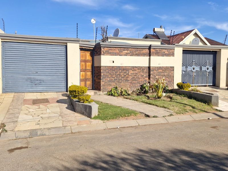 Front exterior view of the property featuring a roller garage door, brick boundary wall with electric fencing, and a paved driveway entrance.