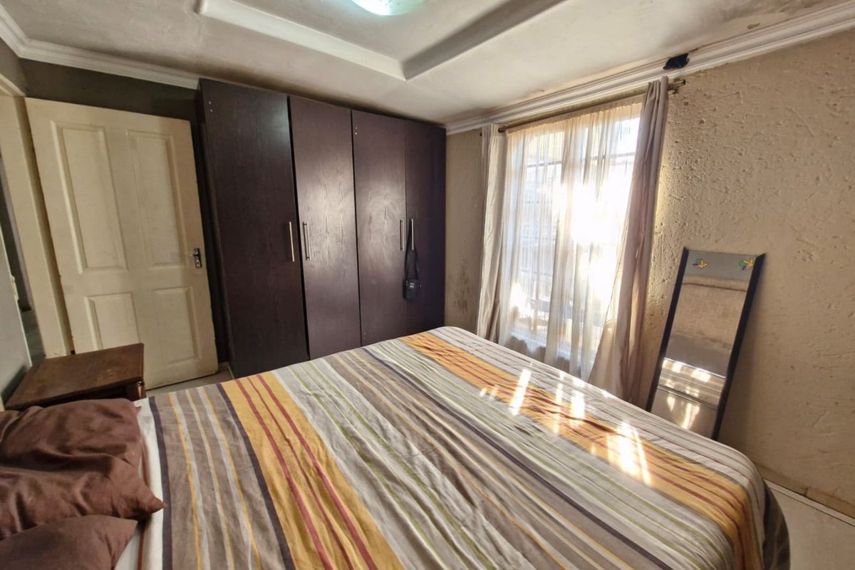 A bedroom featuring a built-in wardrobe and tray ceiling, currently showing signs of wear including wall and ceiling surface damage.