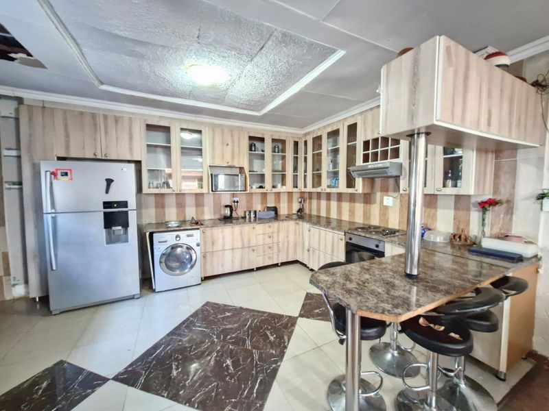 A functional kitchen featuring laminate cabinetry, granite countertops, a breakfast bar, and integrated appliances, with some visible ceiling damage.