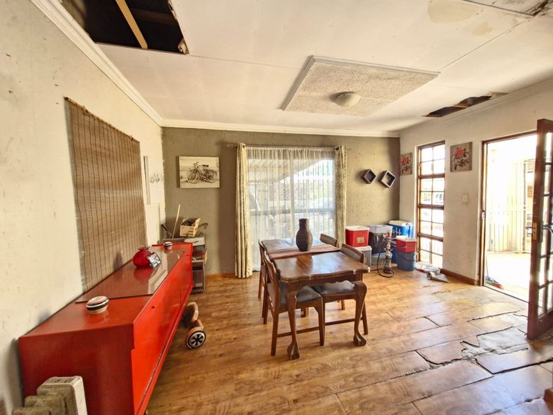 Living area featuring timber flooring and access to an outdoor space, currently requiring significant ceiling and flooring repairs.