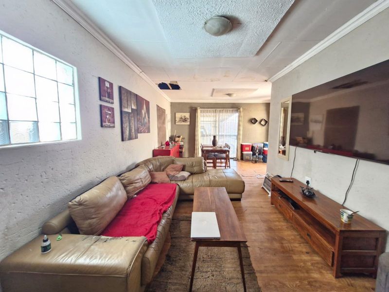 Open plan living and dining area featuring laminate flooring, coving, and a glass block window, requiring ceiling and wall repairs.