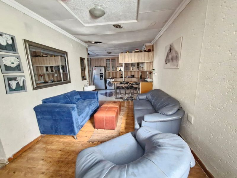 Open-plan living and kitchen area featuring laminate flooring and built-in cabinetry, currently showing significant signs of ceiling water damage and wear.