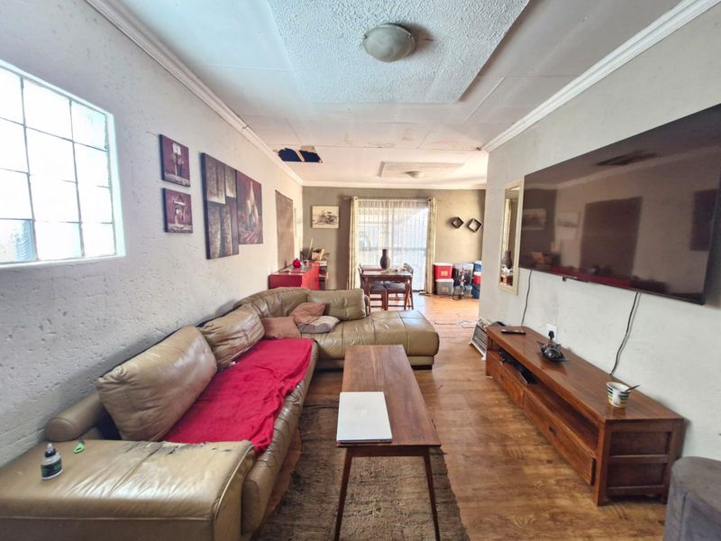 Open plan living and dining area featuring laminate flooring and textured walls, currently requiring ceiling repairs and general maintenance.