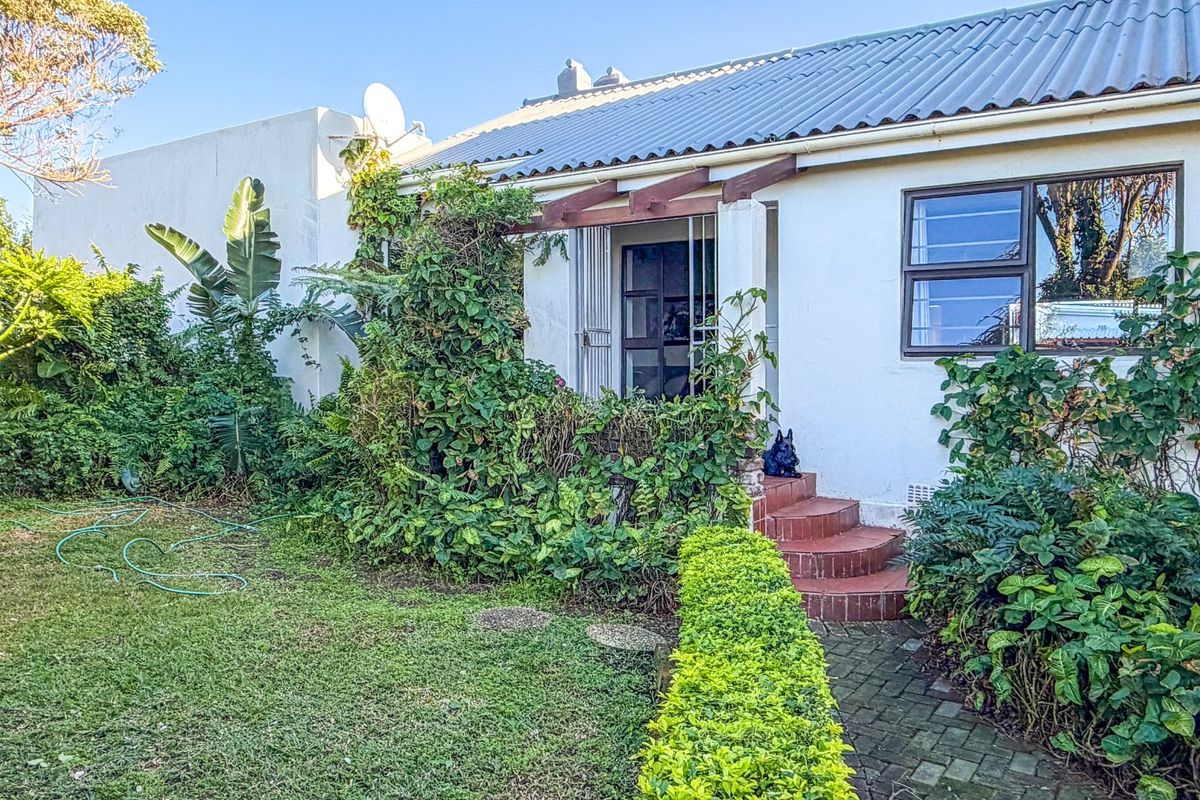 Rear exterior view of the house featuring a corrugated metal roof, brick entrance steps, and a timber pergola, surrounded by established garden landscaping.