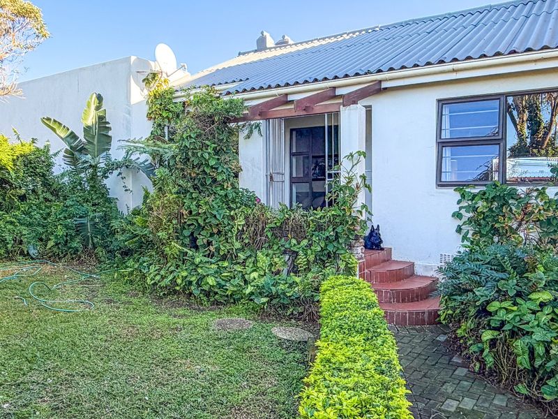 Rear exterior view of the house featuring a corrugated metal roof, brick entrance steps, and a timber pergola, surrounded by established garden landscaping.