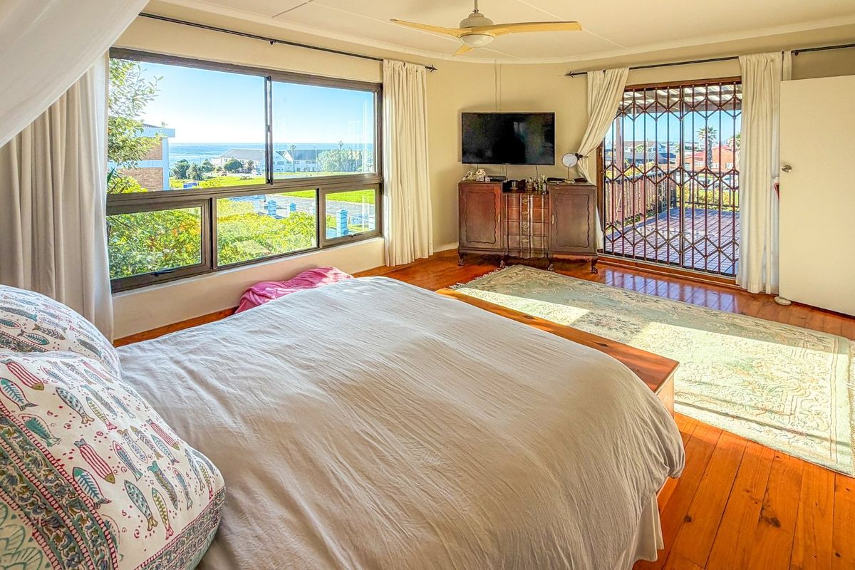 Spacious bedroom featuring polished hardwood flooring, a ceiling fan, and large windows with access to an outdoor balcony area.