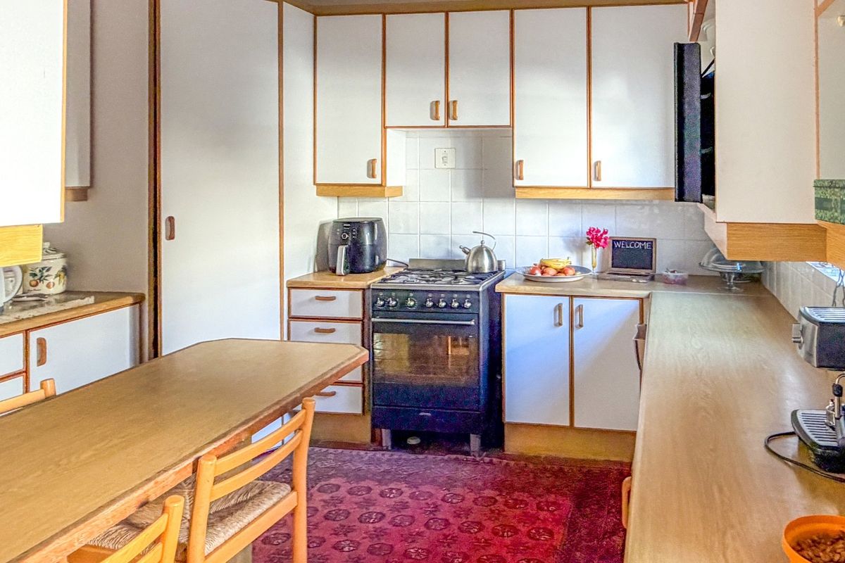 A functional kitchen featuring white cabinetry with wood trim, a gas stove, and tiled backsplash, offering a classic layout with ample counter space.