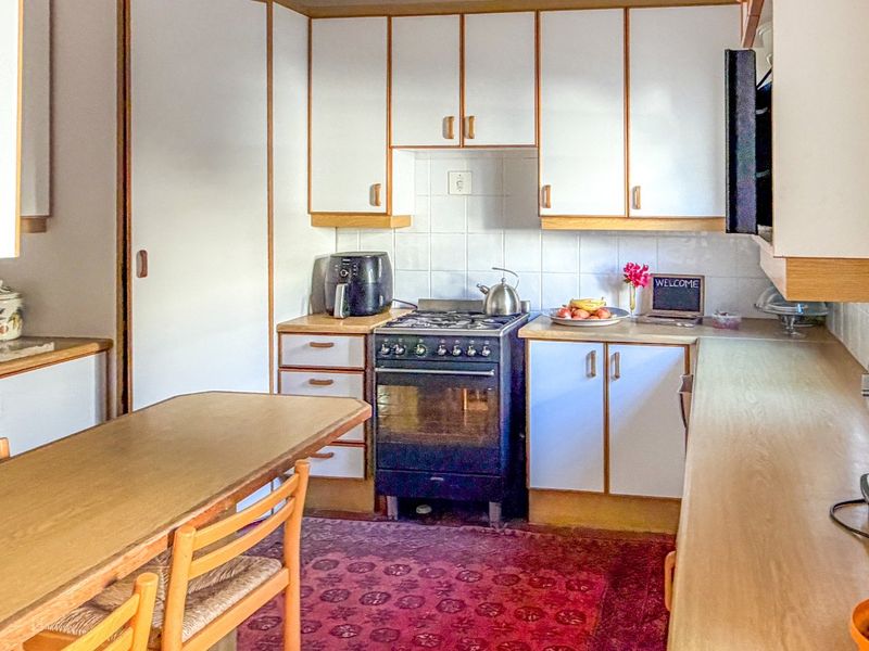 A functional kitchen featuring white cabinetry with wood trim, a gas stove, and tiled backsplash, offering a classic layout with ample counter space.