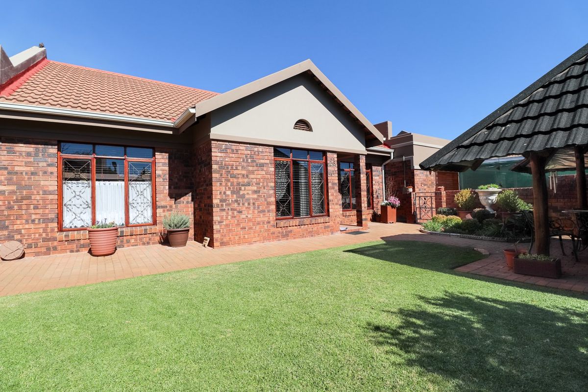 A well-maintained rear exterior view of the townhouse featuring a brick facade, paved patio area, manicured lawn, and a charming thatched gazebo.