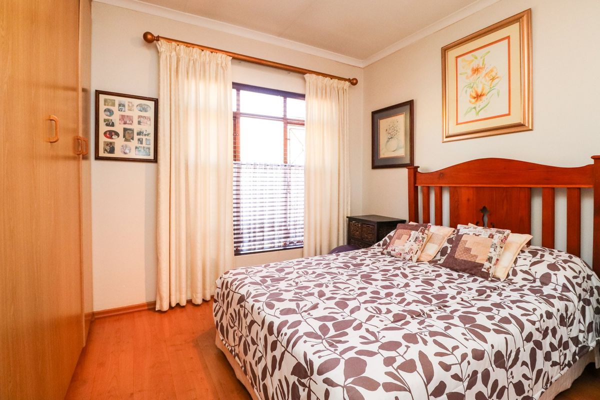 A cozy bedroom featuring laminate flooring, a built-in wardrobe, and natural light through a window with fitted blinds.
