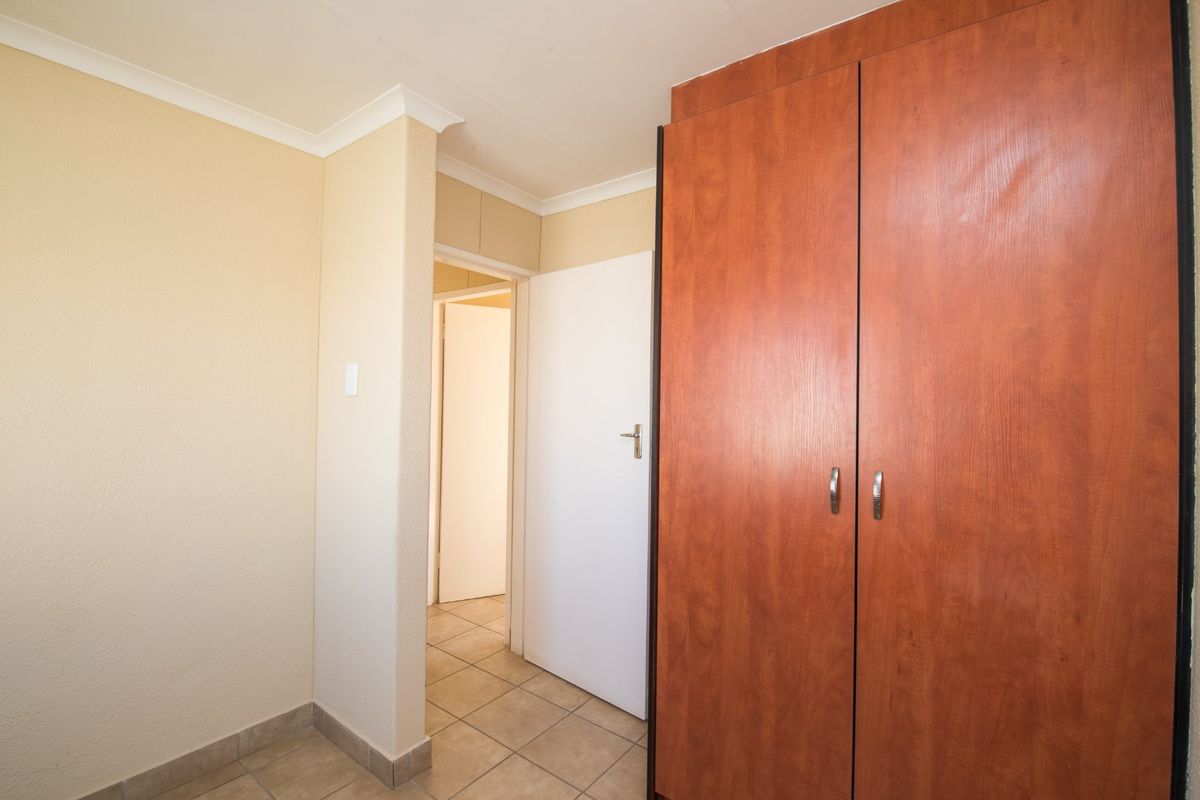 A clean, empty bedroom featuring tiled flooring and a large built-in wooden wardrobe, providing a neutral canvas for personalization.