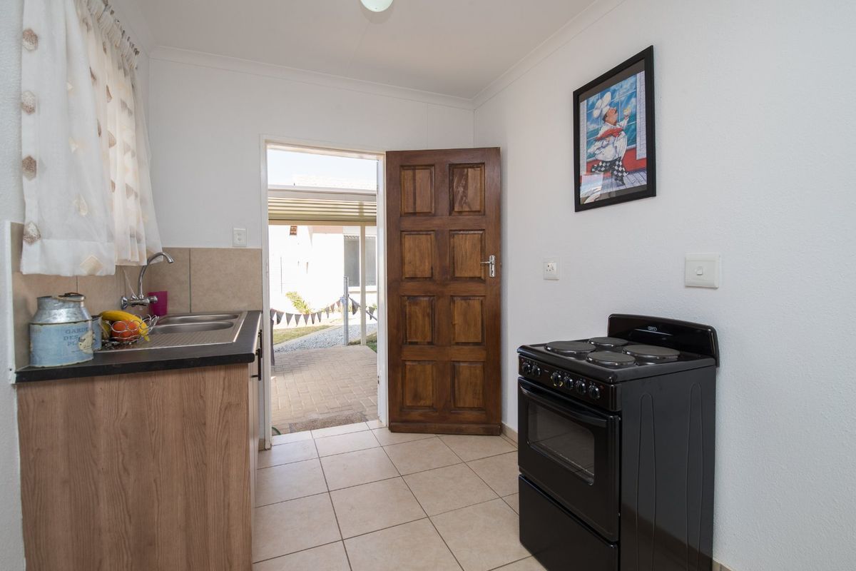 A functional kitchen featuring laminate cabinetry, a stainless steel sink, tiled splashback, and a freestanding electric stove, with direct access to an outdoor patio area.