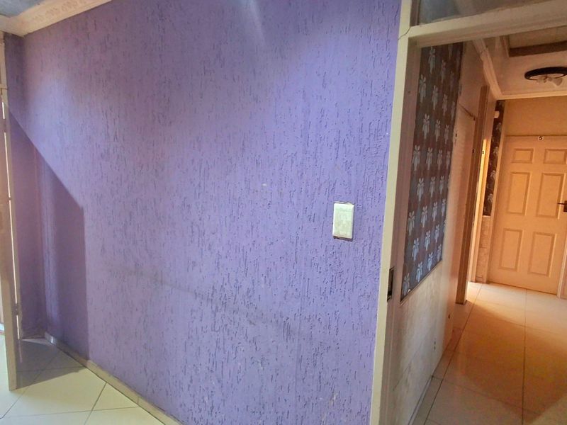 An empty hallway featuring textured purple walls, tiled flooring, and access to internal rooms through standard doors.