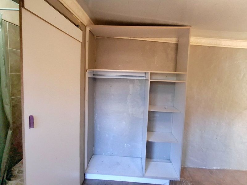 An unfinished bedroom space featuring a built-in wardrobe, wall-mounted basin, and exposed wiring, requiring cosmetic updates and finishing touches.