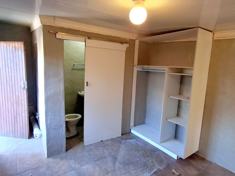 A bedroom featuring tiled flooring, a built-in wardrobe, and an en-suite bathroom with a toilet and basin, requiring cosmetic updates and finishing touches.