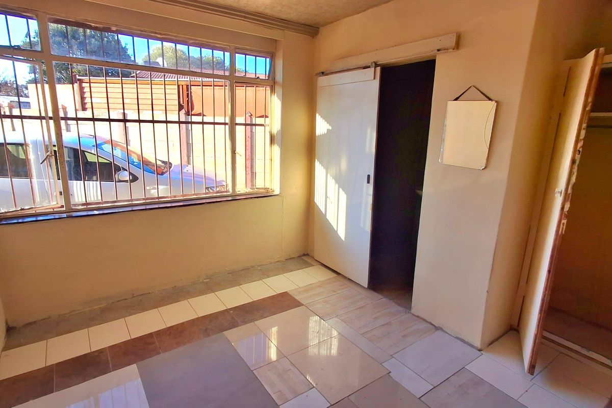 An empty bedroom featuring tiled flooring, security bars on the window, and a built-in cupboard with a sliding door entrance.