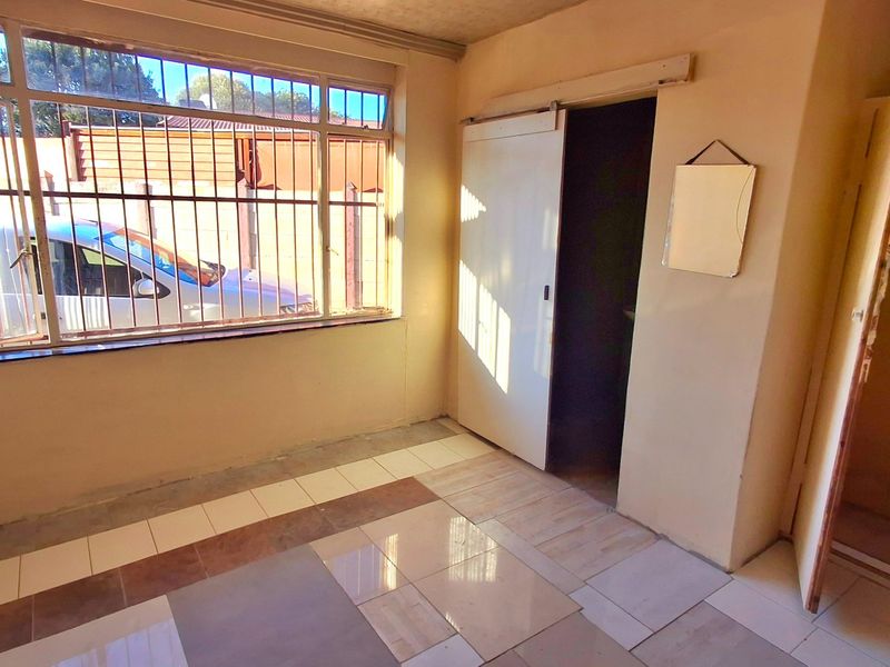 An empty bedroom featuring tiled flooring, security bars on the window, and a built-in cupboard with a sliding door entrance.