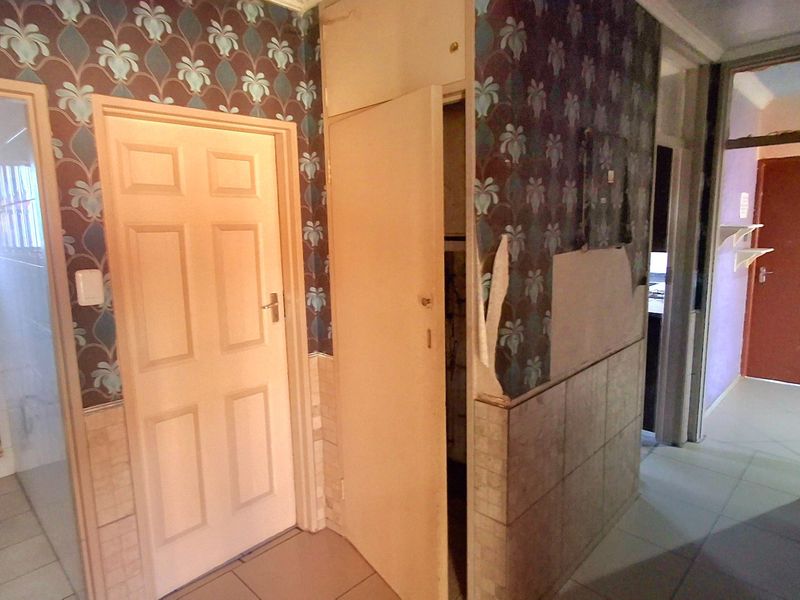 A hallway area featuring tiled flooring and built-in storage, currently requiring cosmetic updates to the wall finishes and wallpaper.
