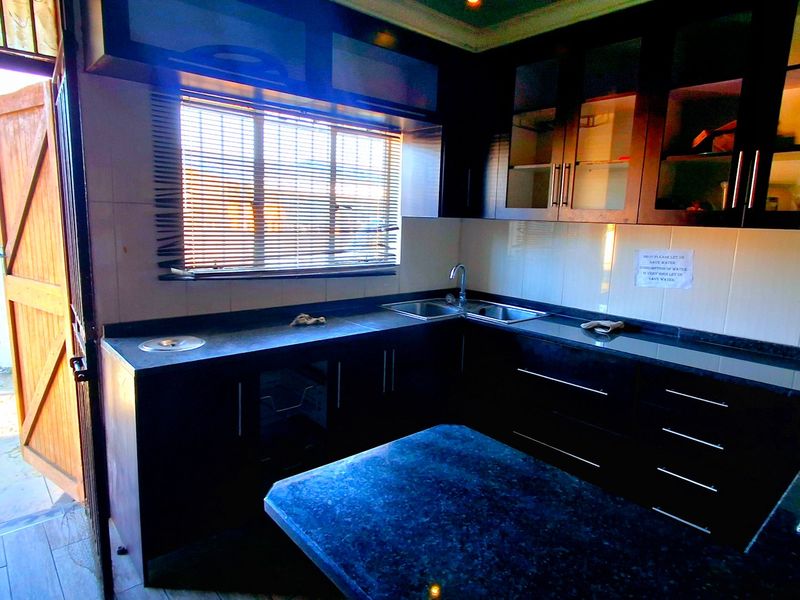 A functional kitchen featuring dark wood cabinetry, laminate countertops, a double bowl sink, and a built-in hob with direct access to an outdoor area.