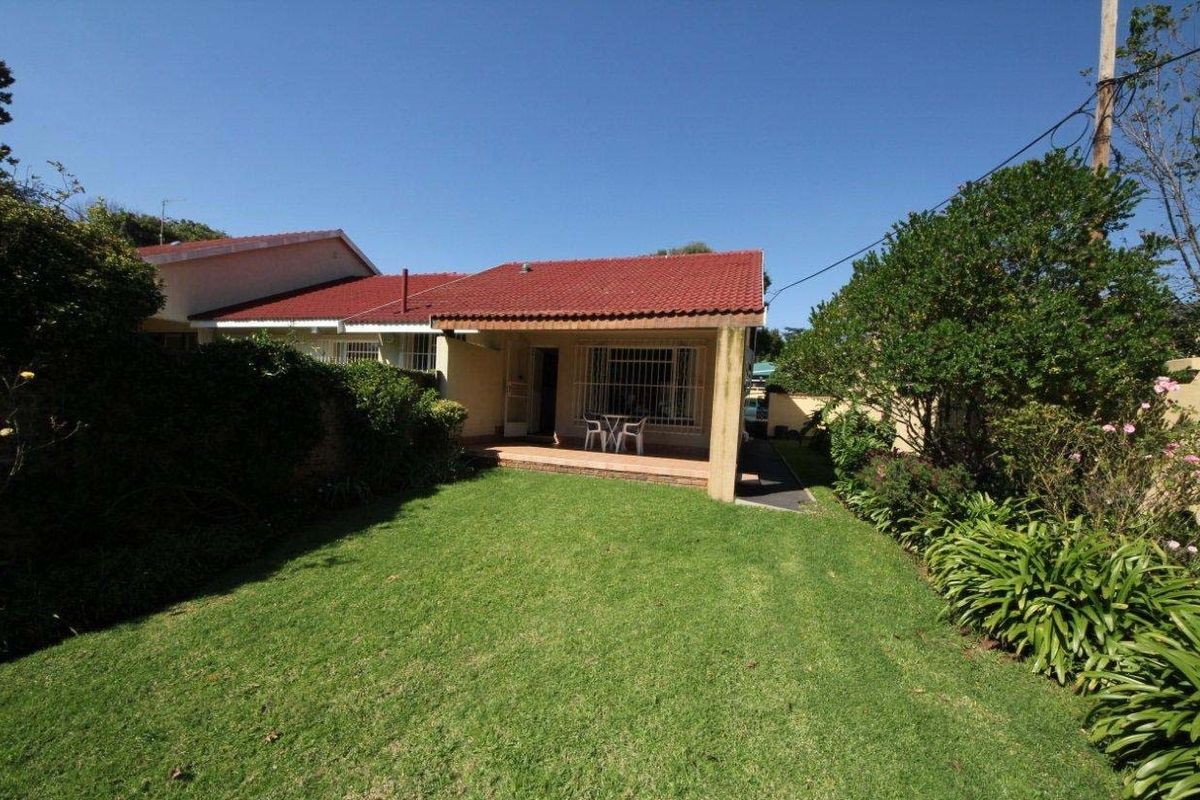Rear view of the property featuring a covered patio, a well-maintained lawn, and established garden borders.