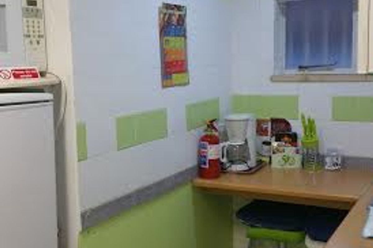 A compact kitchen area featuring a built-in breakfast bar, tiled splashback, and recessed lighting, currently showing signs of dated finishes.