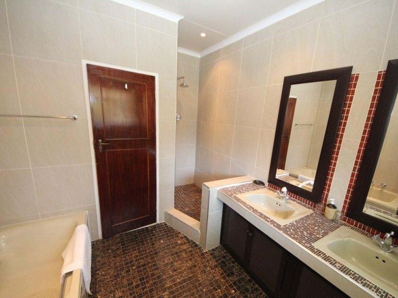 A spacious bathroom featuring a double vanity with mosaic tile countertops, a built-in bathtub, and a separate walk-in shower with neutral wall tiling.