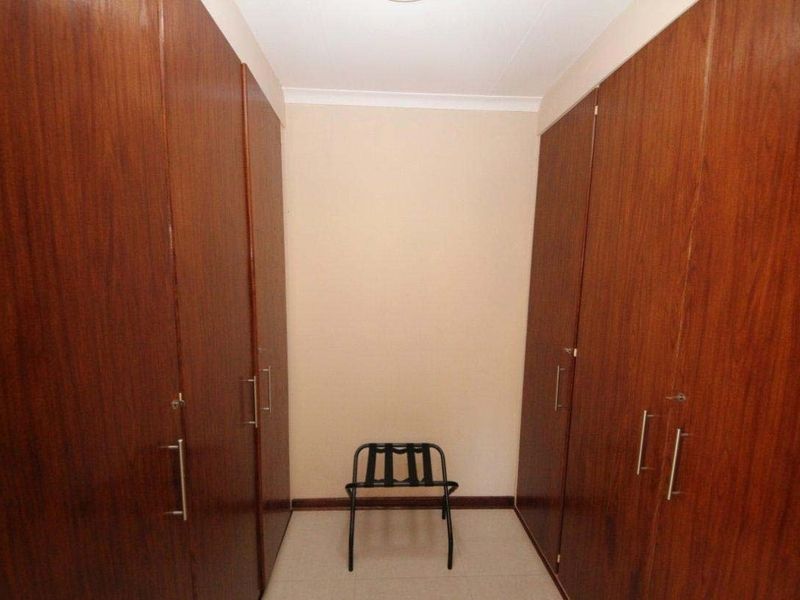 A functional dressing area or bedroom space featuring extensive floor-to-ceiling built-in wooden cupboards providing ample storage.