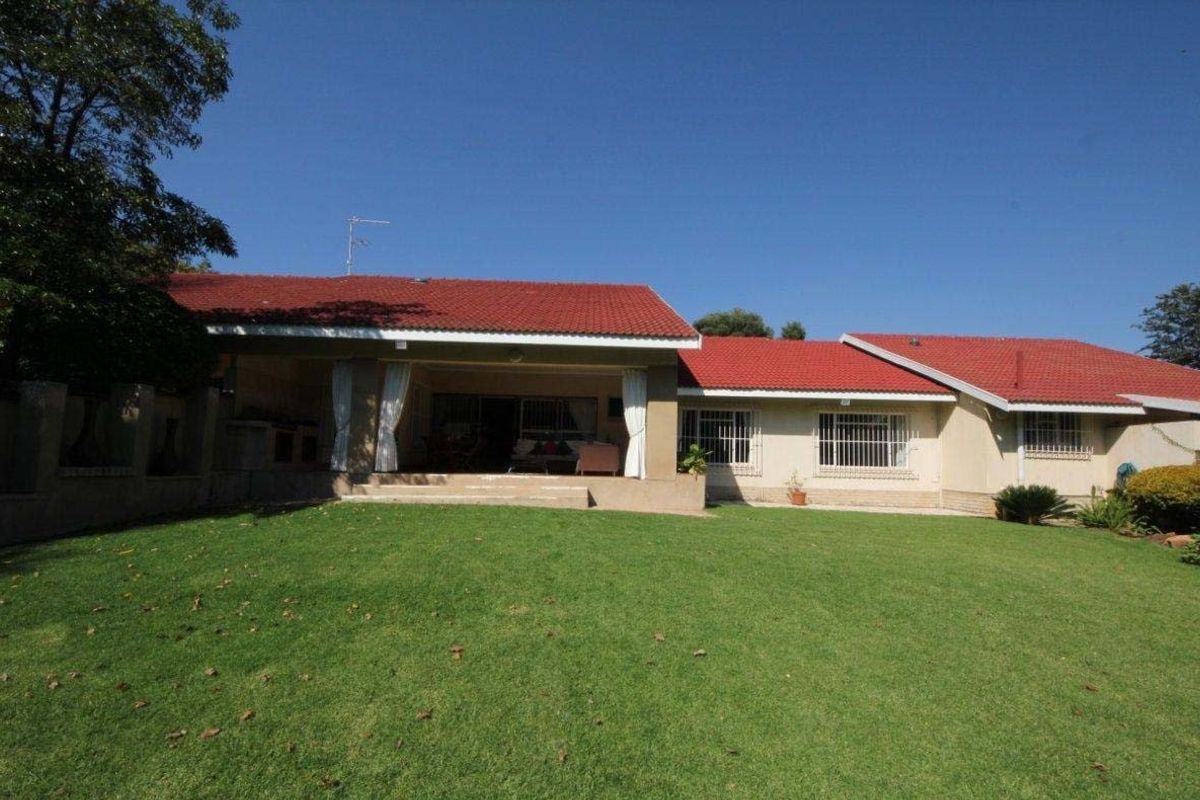 Rear view of the house featuring a red tiled roof, a spacious lawn, and a covered patio area with security bars on the windows.