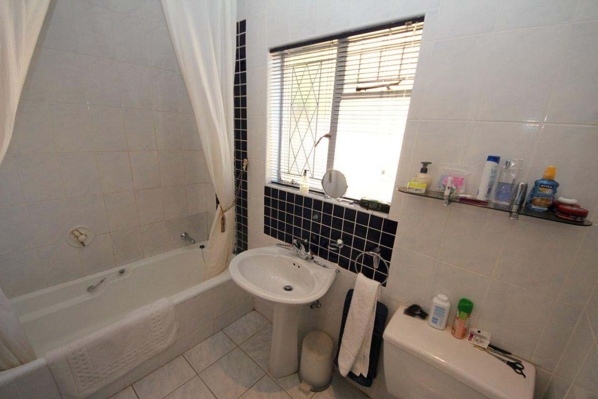 A functional bathroom featuring a pedestal basin, bathtub with shower curtain, and tiled finishes, including a window with security bars.