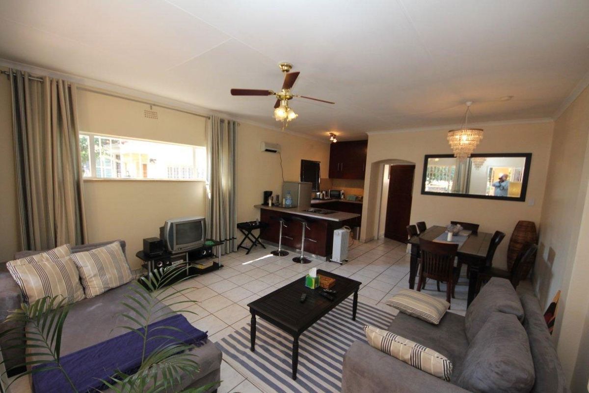 Open-plan living and dining area featuring ceramic floor tiles, a ceiling fan, and an integrated kitchen with a breakfast bar.