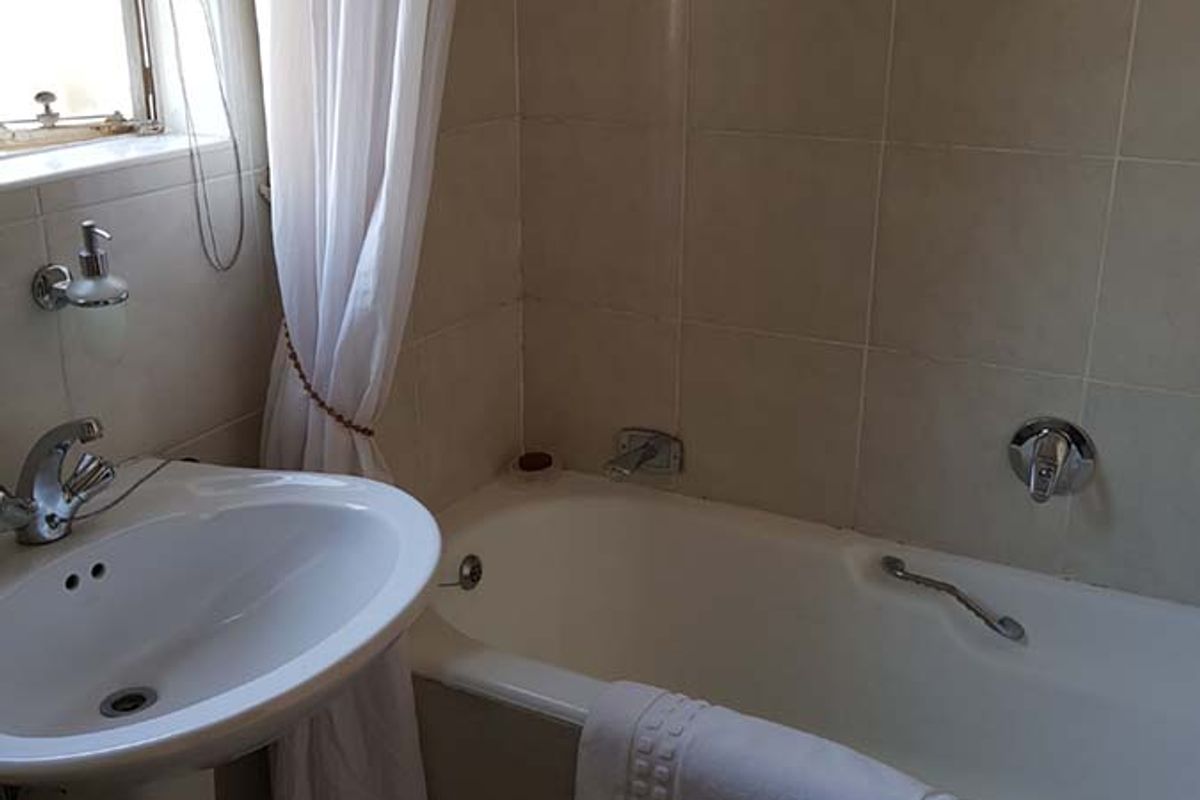 A functional bathroom featuring a pedestal basin, bathtub with shower mixer, and neutral wall and floor tiling.