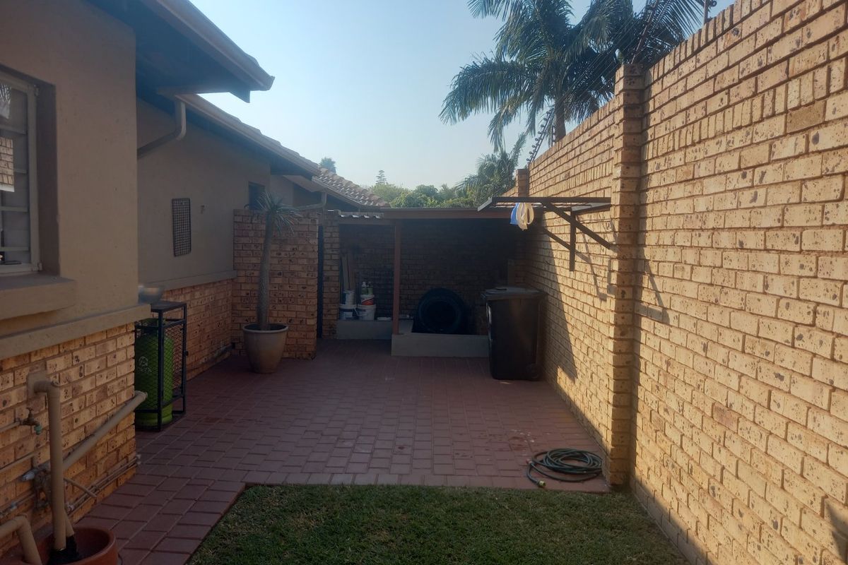 A private rear courtyard featuring paved flooring, a brick boundary wall with electric fencing, and a covered utility storage area.
