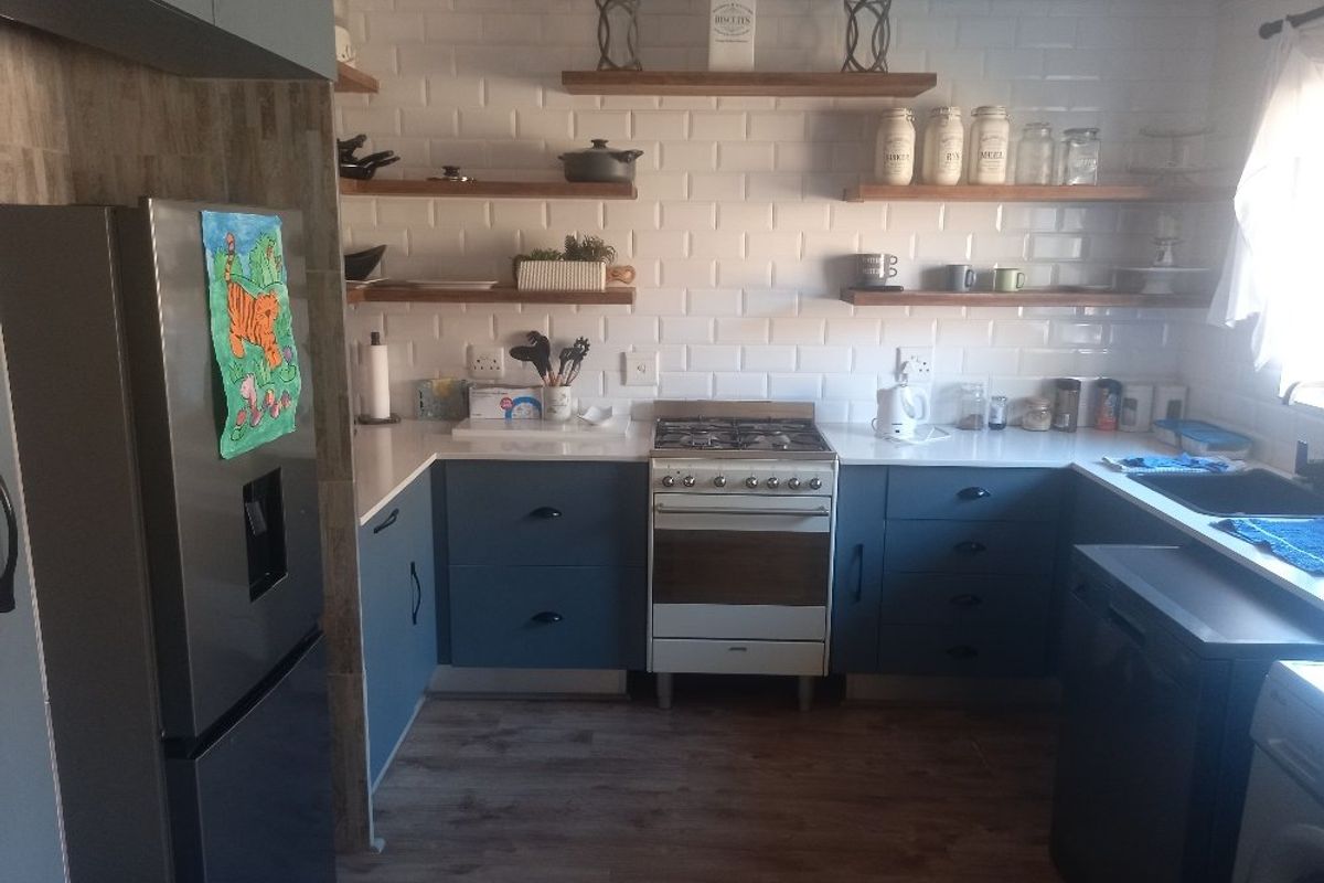 A well-maintained kitchen featuring modern blue cabinetry, white subway tile backsplash, floating timber shelving, and a gas stove with quartz countertops.