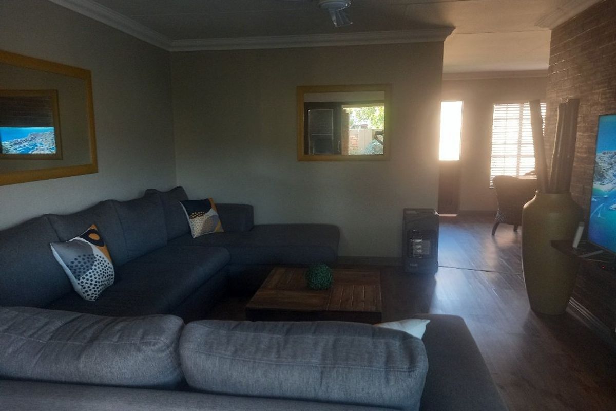 A living room featuring a brick accent wall, laminate flooring, and a ceiling fan, with an open layout leading toward a bright rear entrance.