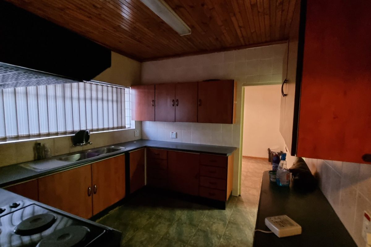 A functional kitchen featuring timber ceiling paneling, laminate cabinetry, dark countertops, and an integrated electric hob with an overhead extractor fan.