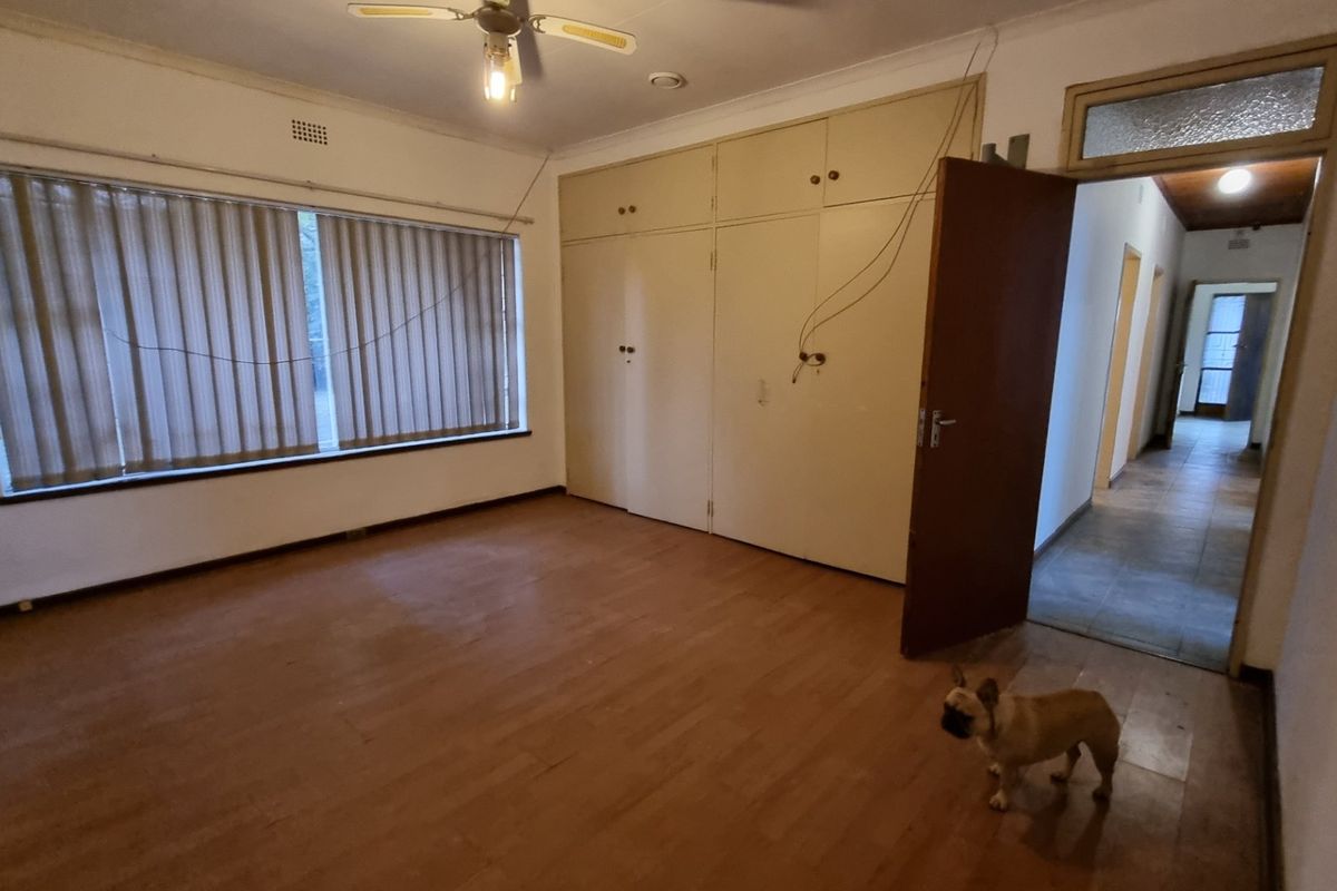 A spacious bedroom featuring built-in cupboards, laminate flooring, and a ceiling fan, offering a blank canvas for renovation and modernization.