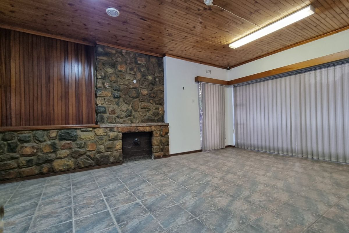Spacious living area featuring a prominent stone fireplace, timber-clad ceiling, and tiled flooring, offering a blank canvas for renovation.