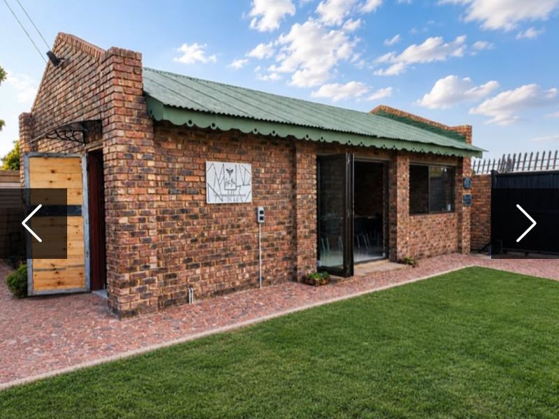 A well-maintained rear exterior view of a face brick building featuring a corrugated metal roof, bi-fold doors, and a neat garden area.