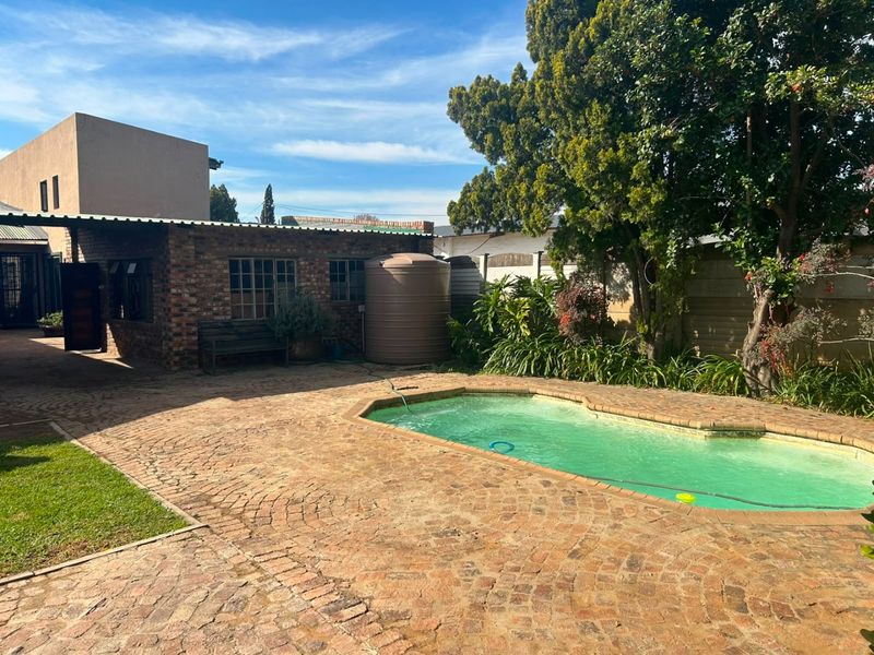 Outdoor pool area featuring brick paving, a swimming pool, and a water storage tank set within a private garden space.