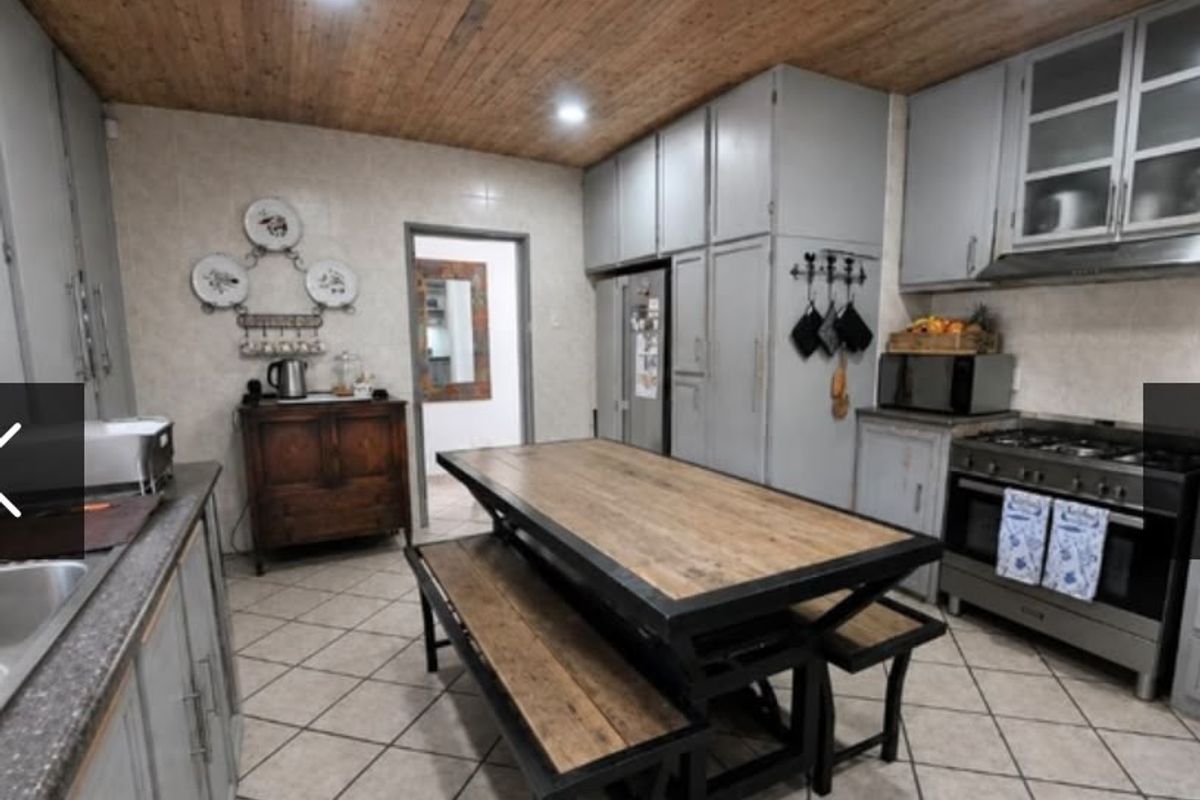 A spacious kitchen featuring grey built-in cabinetry, a gas stove with extractor, tiled flooring, and a distinctive timber-paneled ceiling.