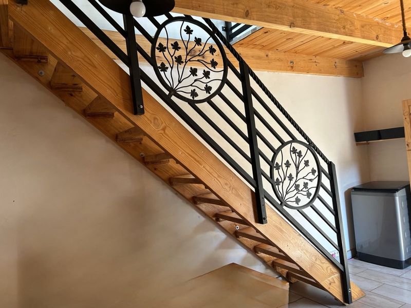 A well-maintained interior hallway featuring a timber staircase with decorative wrought iron balustrades and exposed timber ceiling beams.