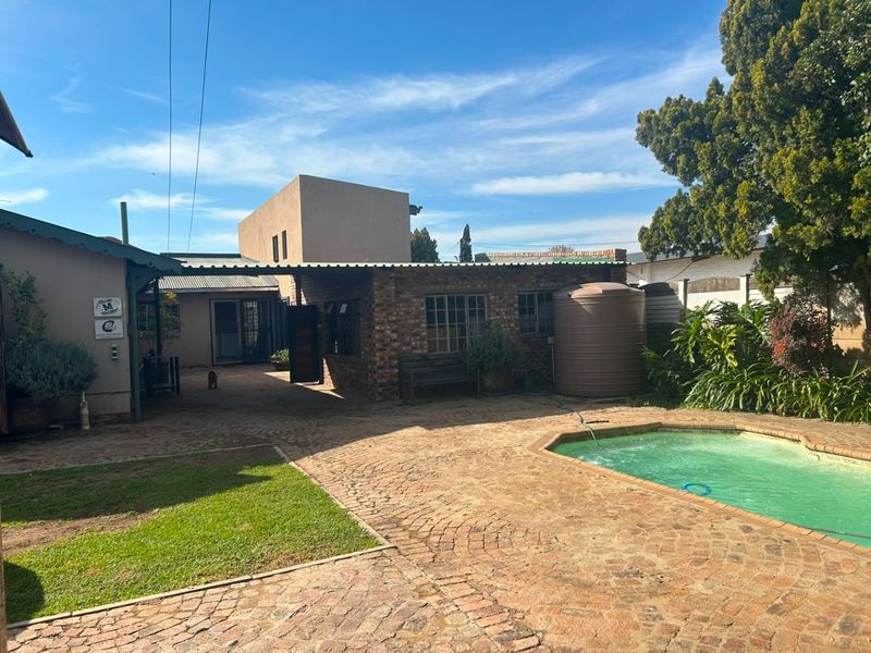 Rear exterior view featuring a swimming pool, brick paved courtyard, and a water storage tank set against the house structure.