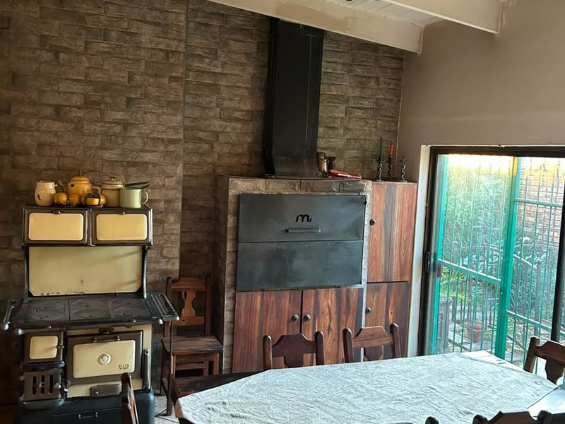 Dining area featuring a stone feature wall, built-in fireplace, exposed beam ceiling, and direct access to the garden through sliding glass doors.