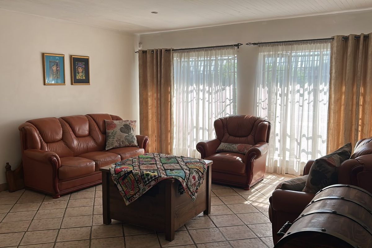 A spacious living room featuring neutral tiled flooring, recessed ceiling lighting, and large windows that allow for ample natural light.